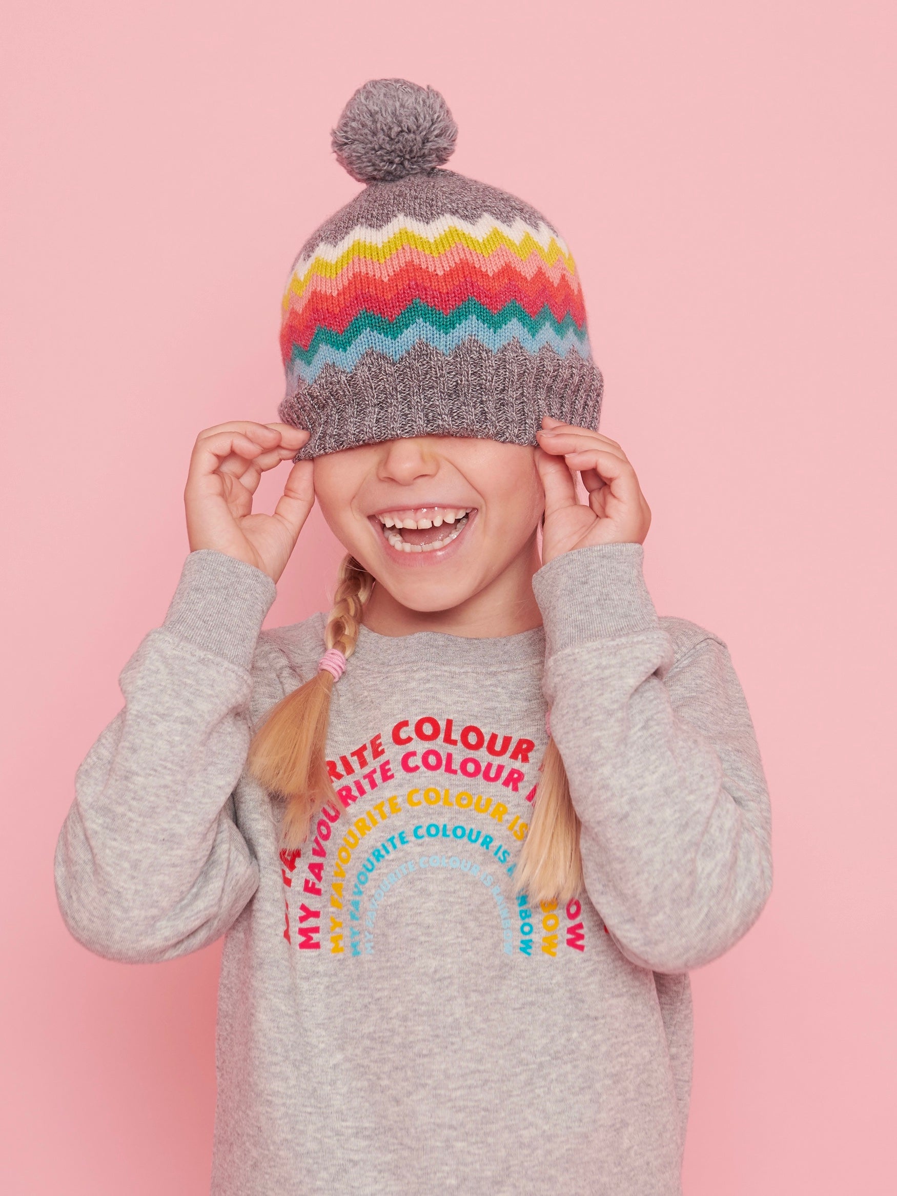 Child wearing a colorful striped beanie and a gray sweater with text on a pink background