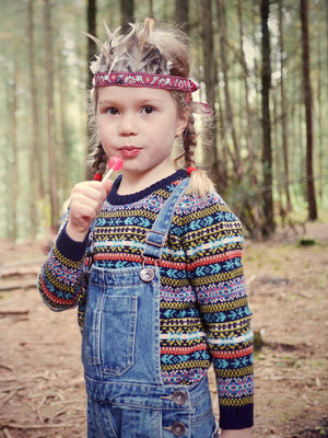 A young girl is wearing 'Explorer' Knitted Jumper by The Faraway Gang and licking a lollypop.