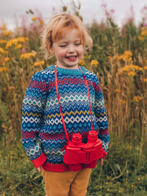 A little girl standing in a field with The Faraway Gang's 'Daydreamer' Knitted Jumper smiling with a camera round her neck.