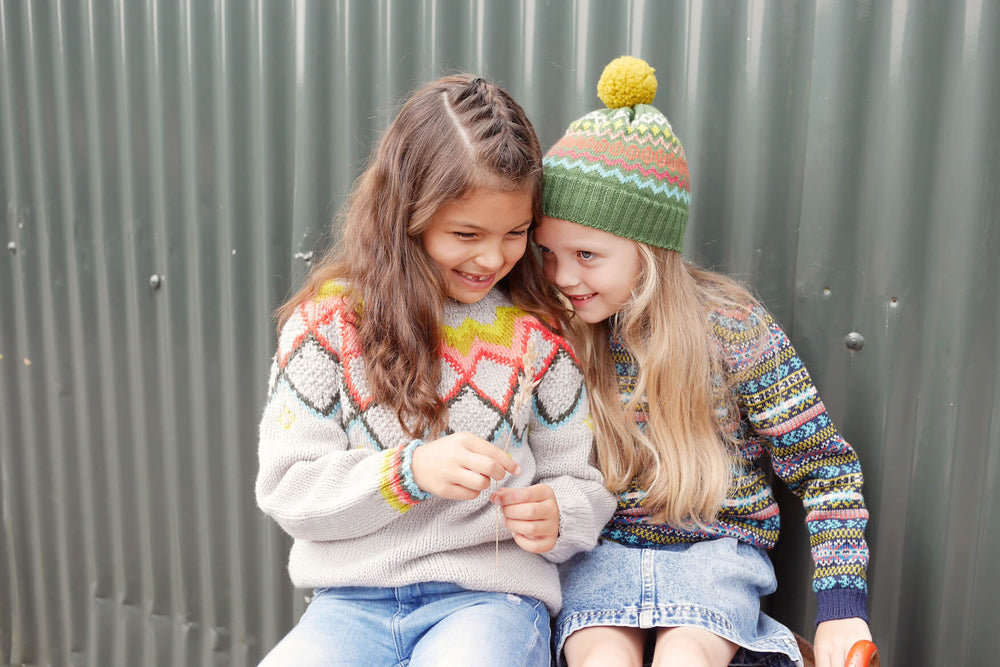 Two girls whispering together wearing The Faraway Gang knitwear.