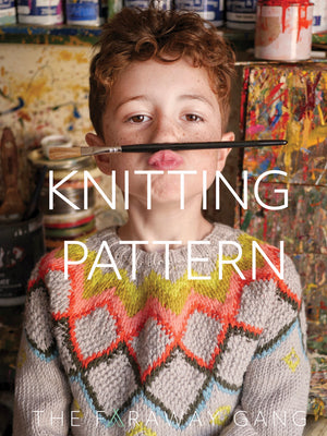 Child wearing a colorful knitted sweater with a paintbrush in front of their face, surrounded by art supplies.