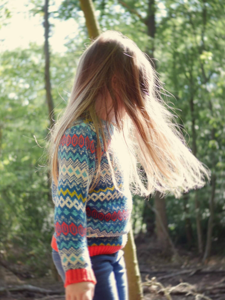 A little girl in a forest, wearing 'The Daydreamer' Jumper from The Faraway Gang with the sun shining through her hair.