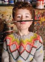 Child with a paintbrush in front of their mouth in an art studio setting
