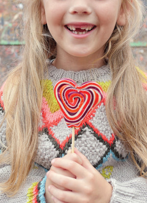 Child wearing a colorful sweater with a heart design, holding a lollipop.