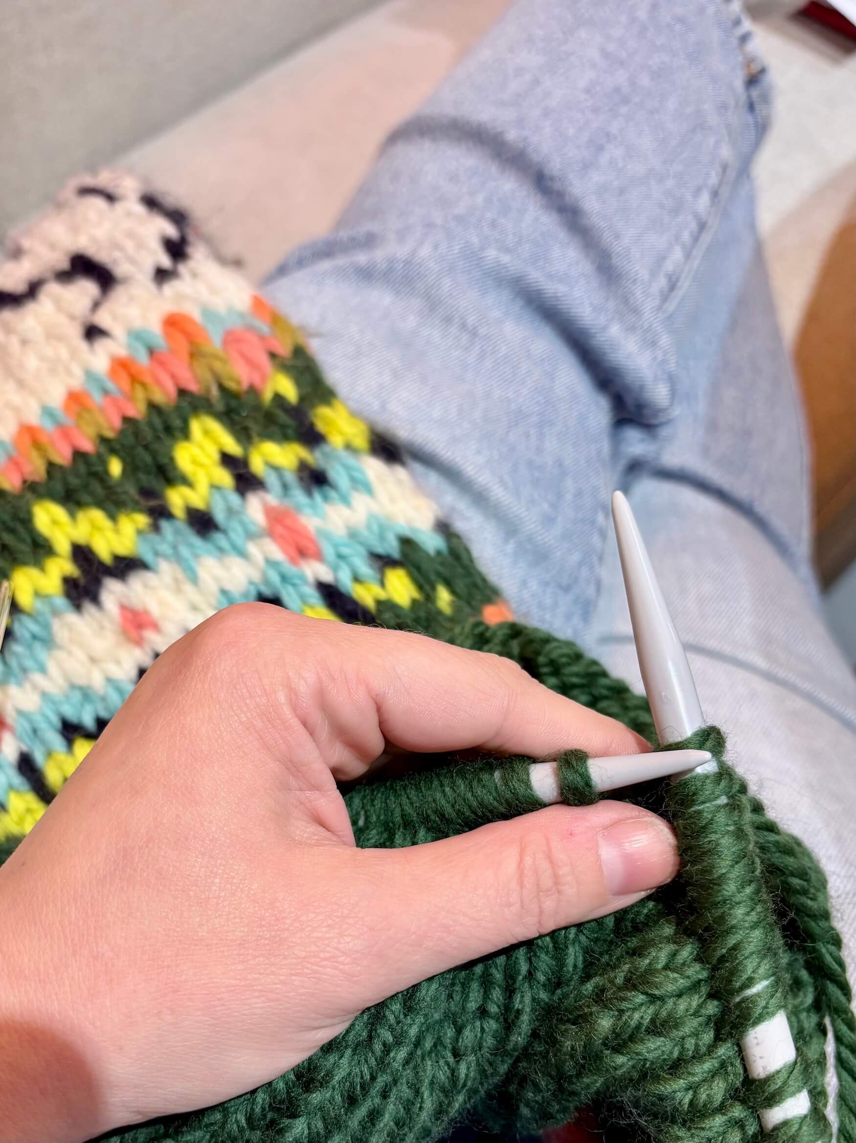 Hand knitting a green fabric with colorful patterns on a couch.