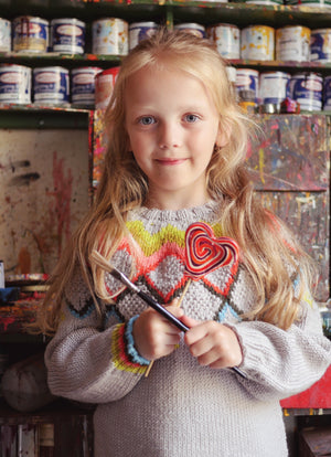 Young girl holding a colorful heart-shaped lolly in an art studio setting