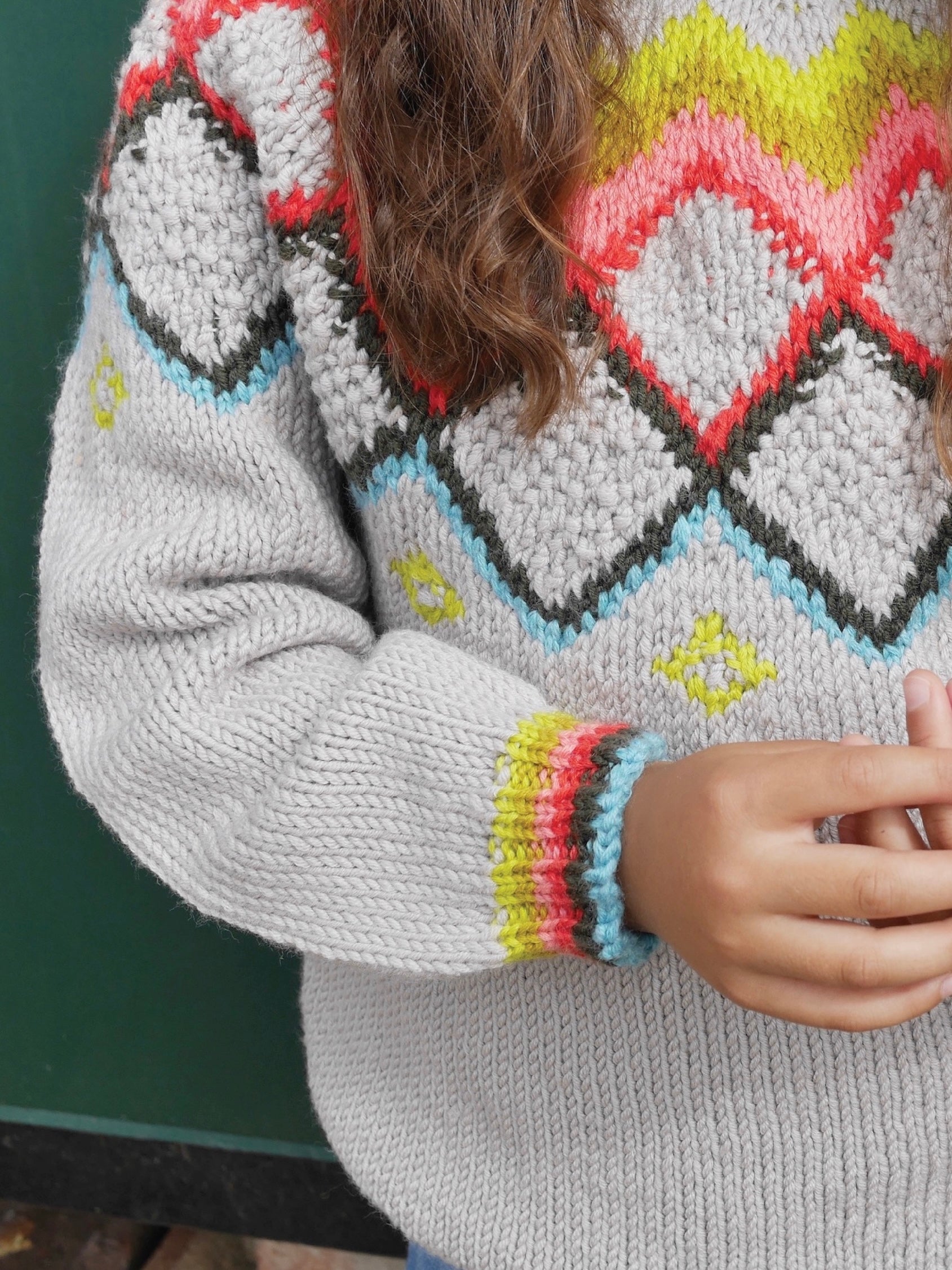 Close-up of a person wearing a gray sweater with colorful diamond pattern