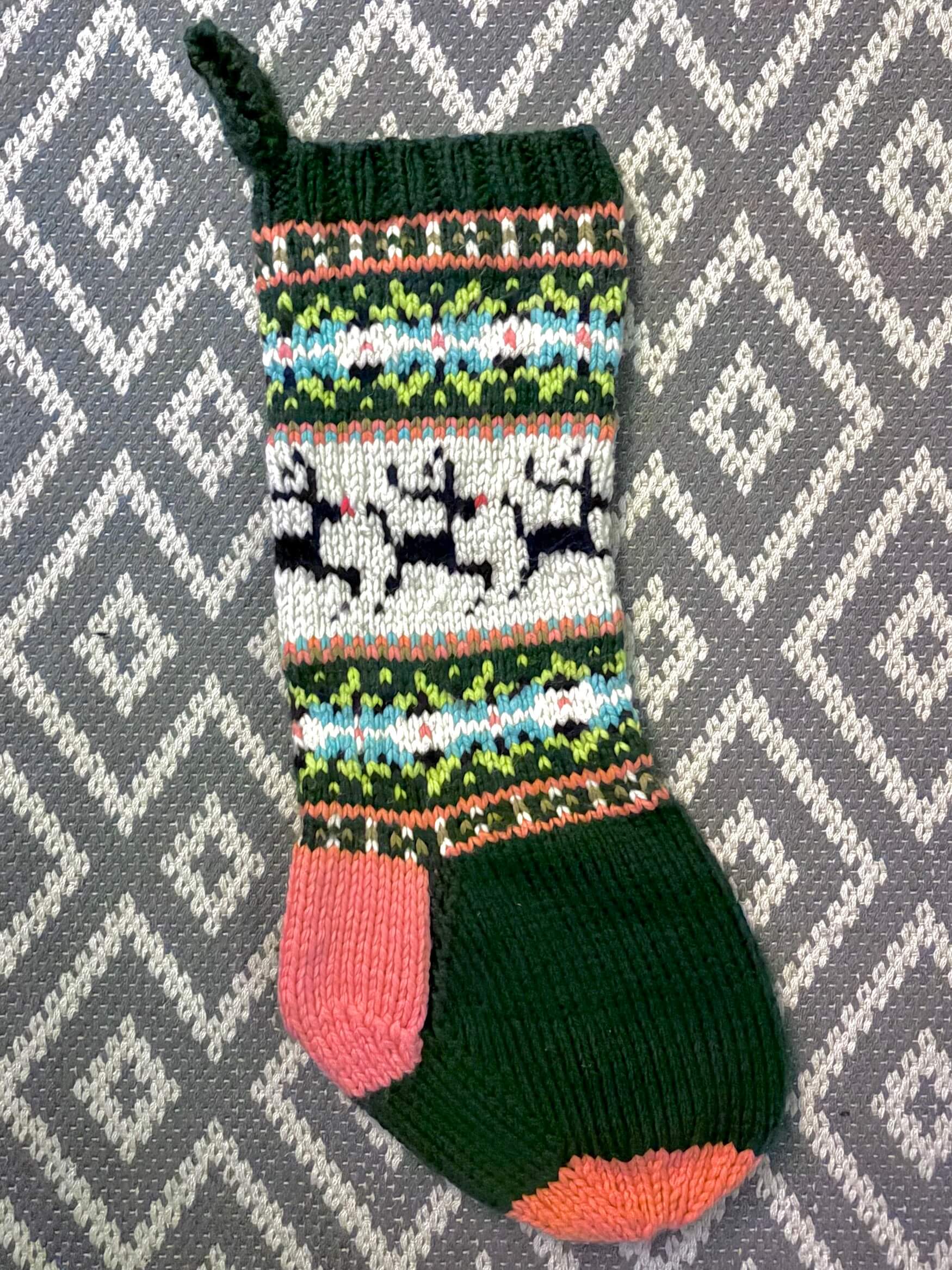 Knitted Christmas stocking with colorful pattern on a gray and white geometric background