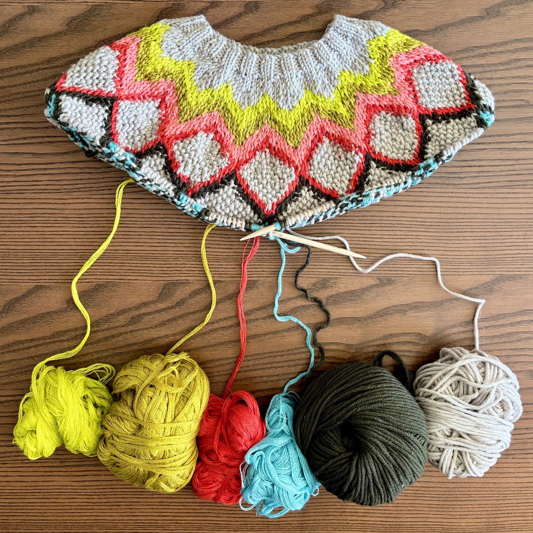 Knitted multicolored garment with yarn balls on a wooden surface