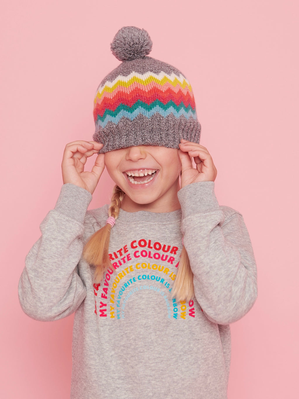 Child wearing a colorful striped beanie and a gray sweater with text on a pink background