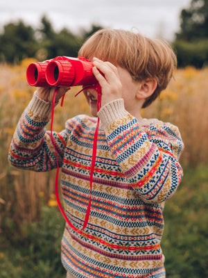 A young boy is wearing 'Explorer' Knitted Jumper by The Faraway Gang and looking through some red binoculars.