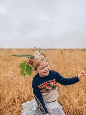 A little girl standing in a field wearing The Faraway Gang's 'Adventurer' Knitted Jumper in colour navy with a homemade cardboard crown on her head.