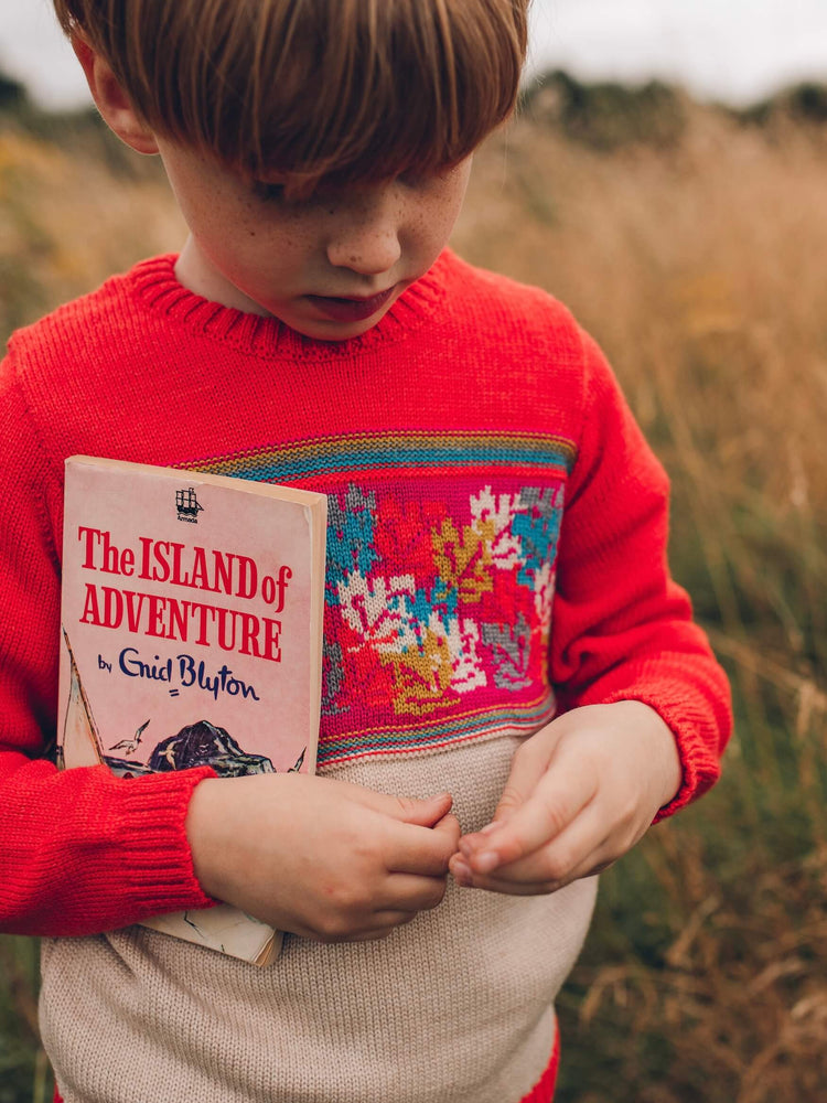 A young boy holding an Enid Blyton book in his hands wearing The 'Adventurer' Knitted Jumper by The Faraway Gang.