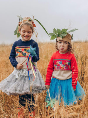 Two little girls standing in a field of tall grass wearing The 'Adventurer' Knitted Jumpers from The Faraway Gang in both colours Navy and Pomegranate..