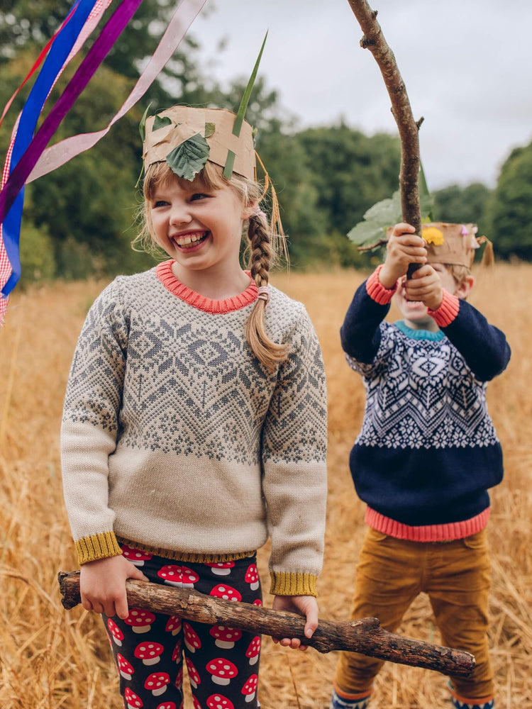 Two young children standing in a field holding a stick while wearing 'The Storyteller' Knitted Jumper from The Faraway Gang.