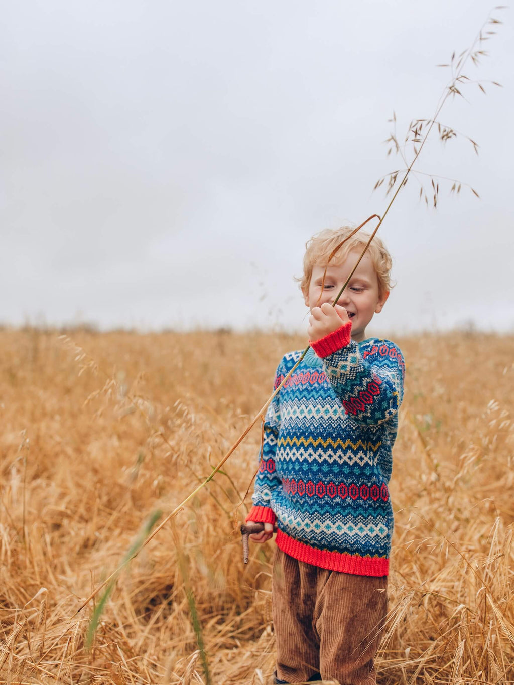 A little boy standing in a field holding some corn wearing 'The Daydreamer' Knitted Jumper from The Faraway Gang.