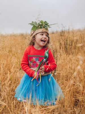 A little girl wearing The 'Adventurer' Knitted Jumper by The Faraway Gang standing in a field holding a wand.