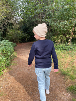 Child wearing the Fisherman hat in cream walking through the woods.