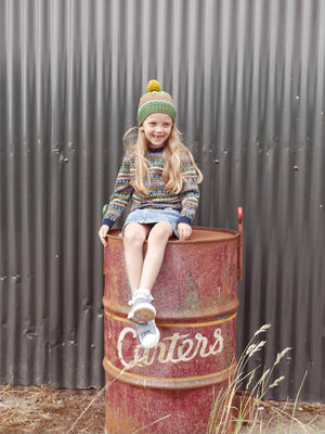 Girl sitting on an oil drum wearing the Voyager knitted hat.