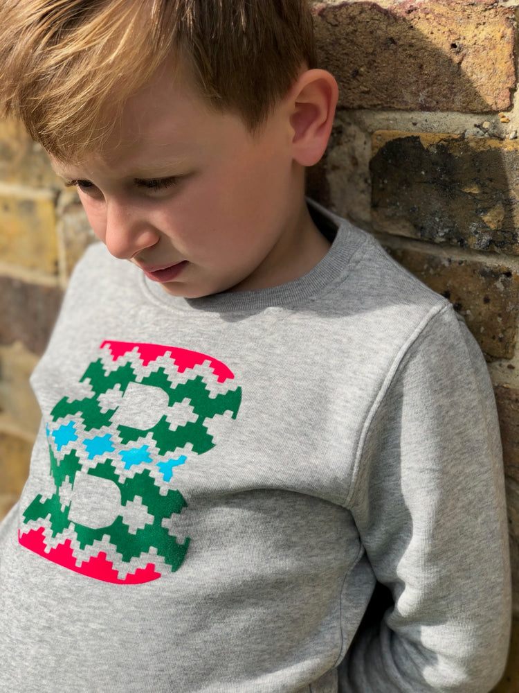 a little boy wearing a 'Narrator' Sweatshirt by The Faraway Gang in grey and leaning against a wall.