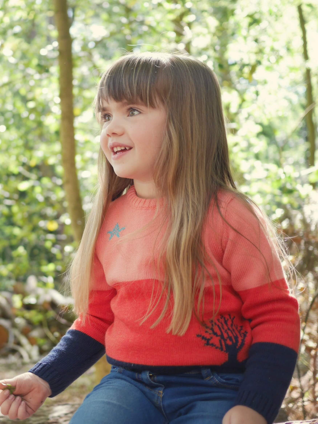 A little girl sat in the woods wearing 'The Stargazer' Jumper by The Faraway Gang.