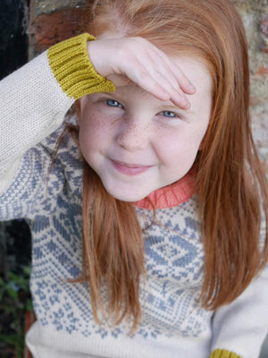 A young girl with a freckled face is smiling in The Faraway Gang's 'Storyteller' Knitted Jumper.