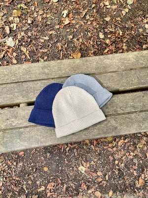 All three colours of the Fisherman Knitted hat lay on a bench.