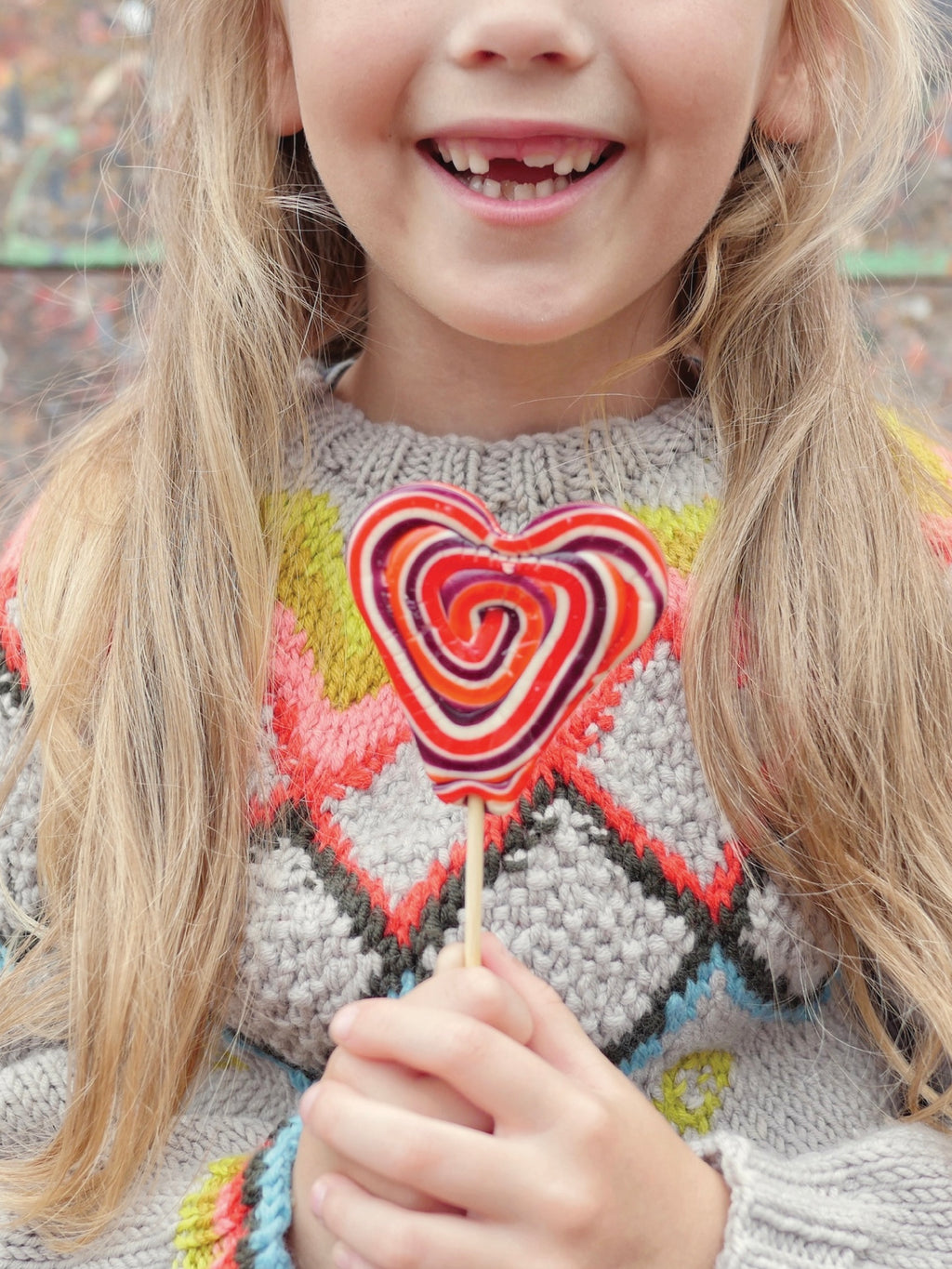 Child wearing a colorful sweater holding a lollipop.