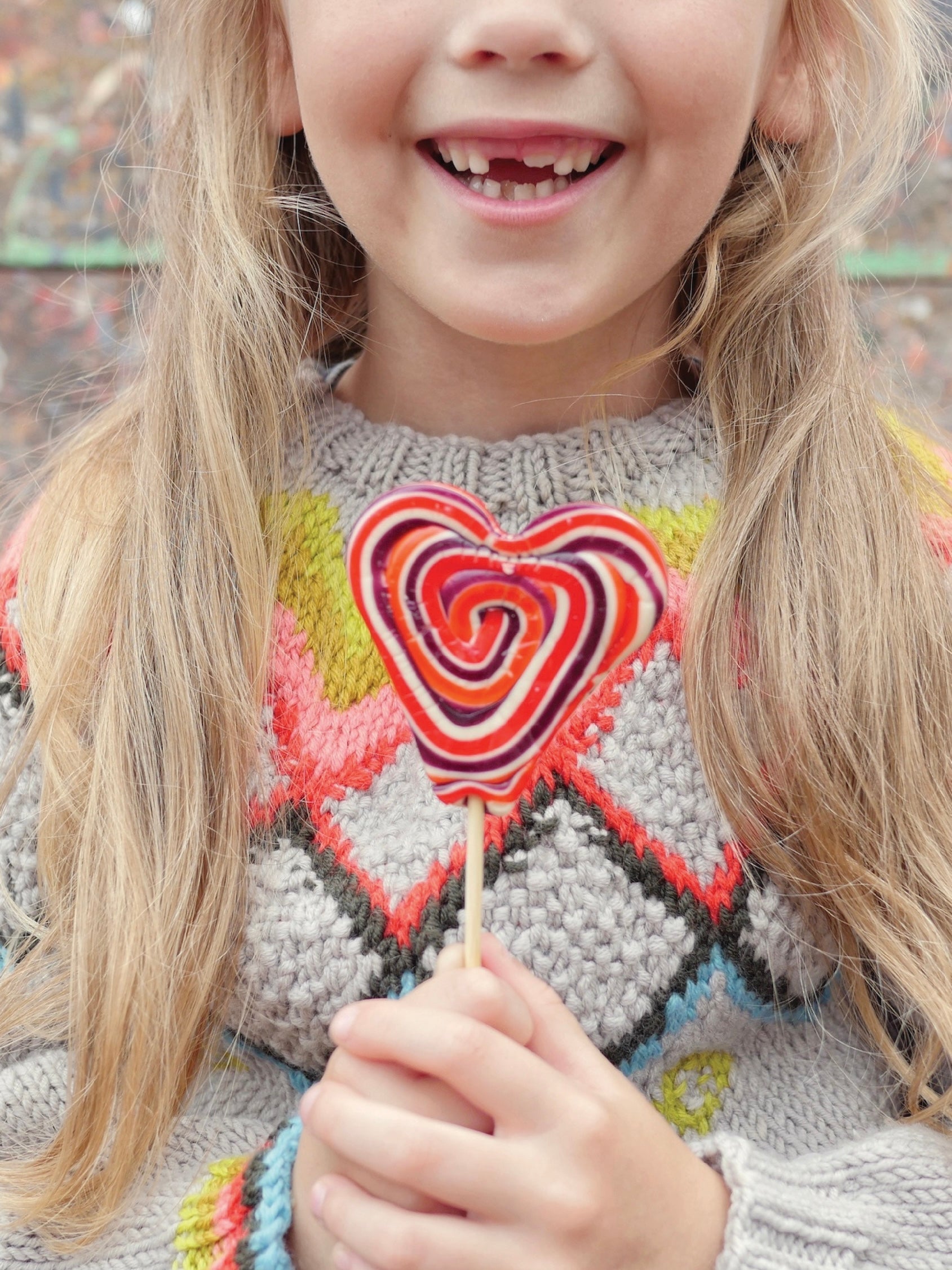 Child wearing a colorful sweater holding a lollipop.